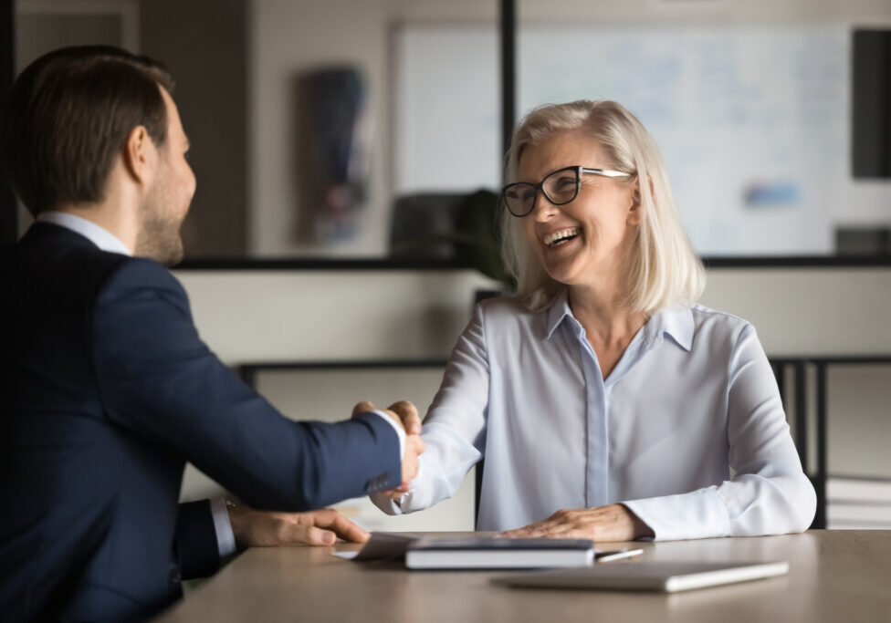 Cheerful elegant mature property investor woman shaking hands with property manager man