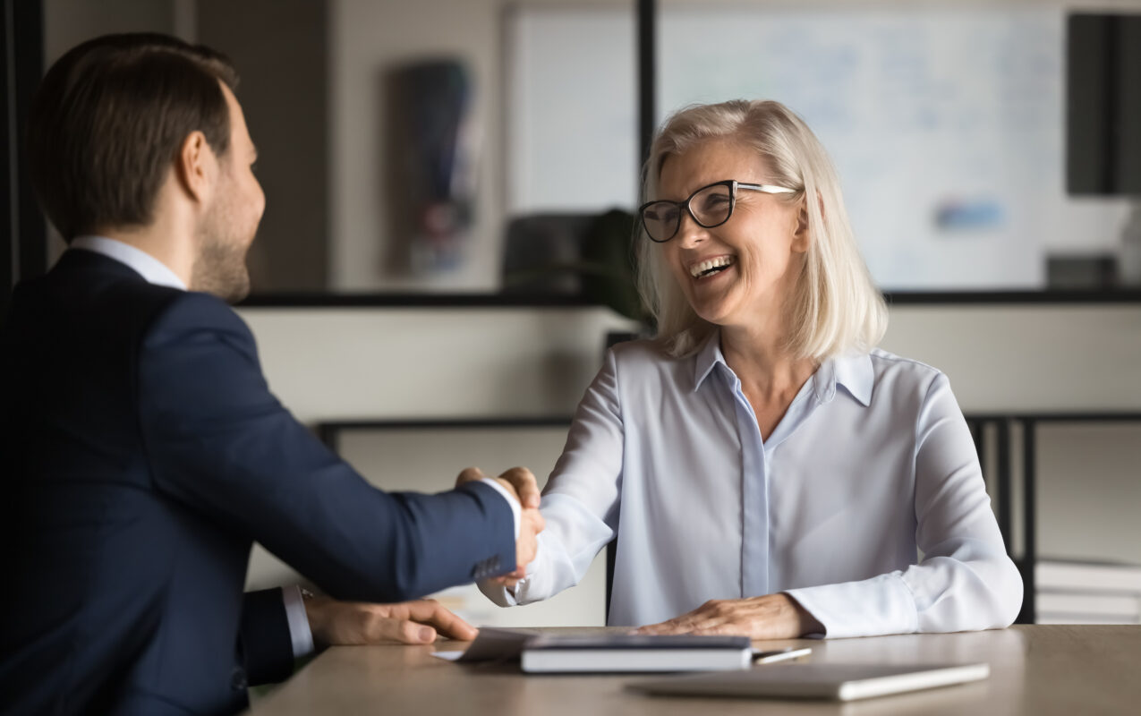 Cheerful elegant mature property investor woman shaking hands with property manager man